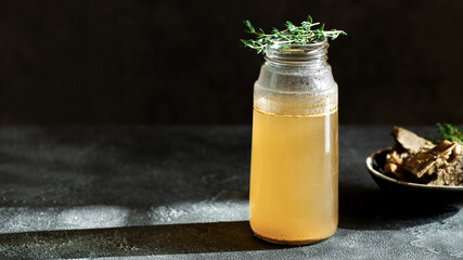 Fresh vegetable bone broth in glass jar with herb on dark gray background. Healthy dieting food are rich in vitamins, collagen and anti-inflammatory amino acids - obrazy, fototapety, plakaty