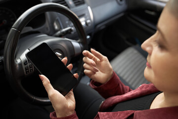 People, age, transportation, modern lifestyle and technolgy concept. High angle view of stylish gray haired mature woman sitting in driver's seat holding smart phone, setting online GPS navigation app