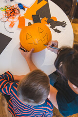 mother with son making pumpkin head at home together