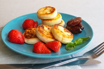 Delicious curd cheesecakes with strawberry berries and dates on a blue platter. The concept of a healthy Breakfast. Close-up,white background
