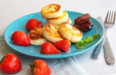 Delicious curd cheesecakes with strawberry berries and dates on a blue platter. The concept of a healthy Breakfast. Close-up,white background.