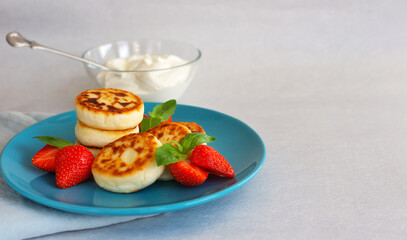 Delicious, homemade cheesecakes made from fresh cottage cheese, on a blue platter, with strawberries. In a bowl of sour cream.Light grey background, selective focus, text space, horizontal