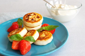 Delicious cottage cheese cheesecakes with strawberry berries and sour cream on a blue platter. The concept of a rich and healthy Breakfast. White background, close up