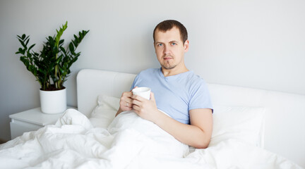 good morning concept - handsome man sitting in bed and drinking coffee