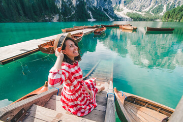 Obraz premium woman in red sundress sitting on wooden stairs looking at lake in mountains