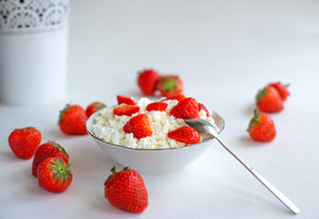 Cottage cheese in a white bowl with strawberries, on a white background, with a teaspoon. Concept of home-made, healthy food, space for text at the top, horizontal cropping