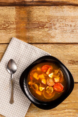 Traditional Thai Tom Yam soup in a black plate on a wooden table on a napkin with a spoon.