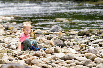 child sat on rocks at waters edge