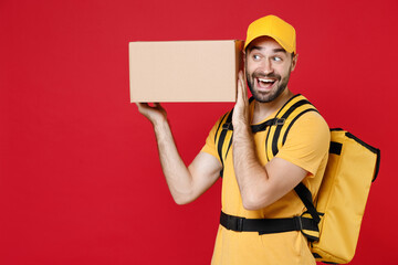 Delivery man in yellow cap t-shirt uniform thermal bag backpack with food hold cardboard box isolated on red background studio Male employee work as courier Service coronavirus covid-19 virus concept