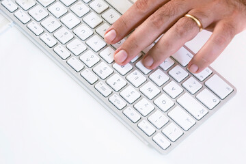 male hand typing on a white keyboard on a white table