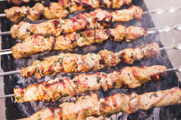 Preparation of shish kebab on barbeque over charcoal. Closeup of grilled meat cooking on metal skewer, smoke. Summer picnic/BBQ. Tasty street food. Traditional eastern dish. Natural bluerred backdrop.