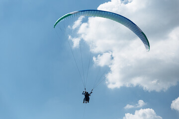 Blue Paraglider flying into the sky with clouds on a sunny day