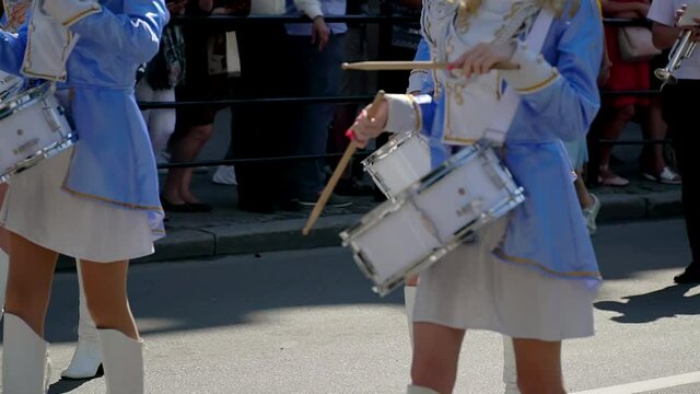 Street performance of festive march of drummers girls in blue costumes on city street. Close-up of female hands drummers are knocking in the drum of their sticks