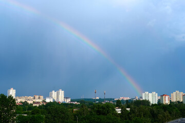 Bright multicolored rainbow on the houses of the city in the blue sky