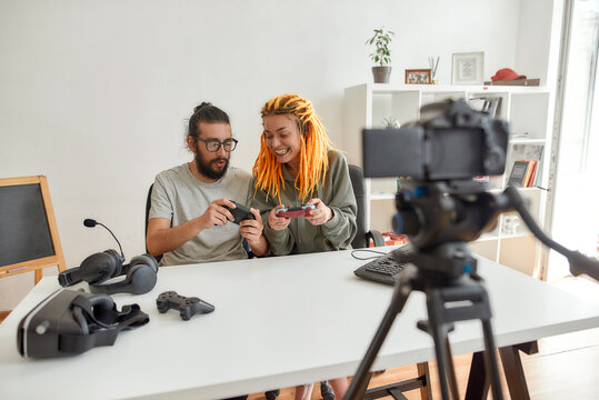 Man and woman using, discussing game controller joystick. Young male and female technology blogger recording video blog or vlog about new gadgets at home