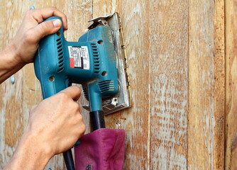 The polished wood working. Carpenter workspace refining the surface of wood board using sand paper grinder. closeup photo of cabinetmaker grinds wooden surface.