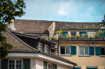 Zurich architecture. The facade of the house, windows with green shutters, brown tile roof. terrace decorated with flowers in pots.