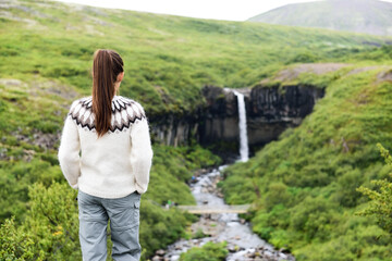 Naklejka premium Iceland. Woman hiking looking at Svartifoss waterfall. Female is visiting famous tourist attraction of Iceland. Spectacular natural landmark on vacation in Skaftafell. Icelandic nature landscape.