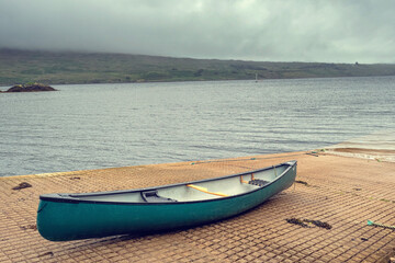One blue canoe on a rump to water. Nobody. Cloudy moody sky. Outdoor activity and sport concept. Toned