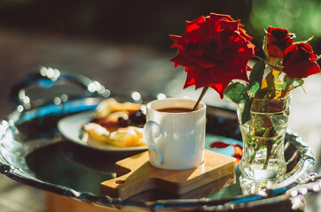 Fototapeta na wymiar Still life shot of breakfast tray silver platter with cup of coffee, roses and pancakes bathed in golden light