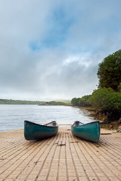 Two blue canoe on rump to water. Nobody. Cloudy sky. Water sports and activity concept. Vertical image.