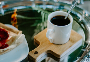 Close up cup of coffee on a wooden saucer on a silver breakfast platter with flower