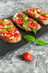 Tasty sandwiches with strawberry, blood orange, soft cheese and basil leaves on roasted wholegrain bread served on black feed board. Healthy delicious breakfast or lunch concept.