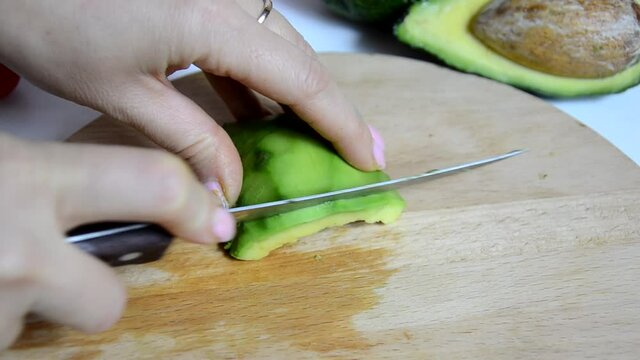 Closeup of female hands cooking with avocado at table in home kitchen. Getting the seed out and cut slices