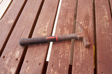 A large rusty hammer with plastic handles against a background of brown old wooden planks.