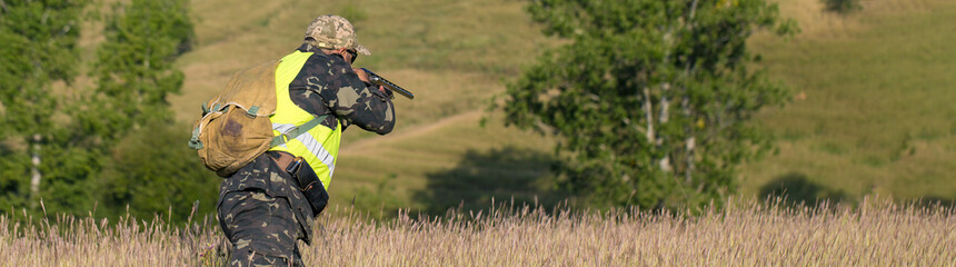 Silhouette of a hunter with a gun in the reeds against the sun, an ambush for ducks with dogs