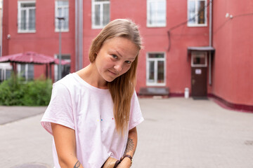 Young beautiful stylish woman sitting on the street on a Sunny summer day. A fashionable girl wears a white tshirt and blue jeans. A woman with long straight hair and tattoo