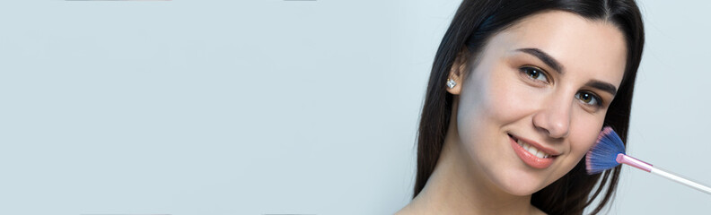 Close-up of a young girl in a light top on a white background making a facial make-up. A pretty...