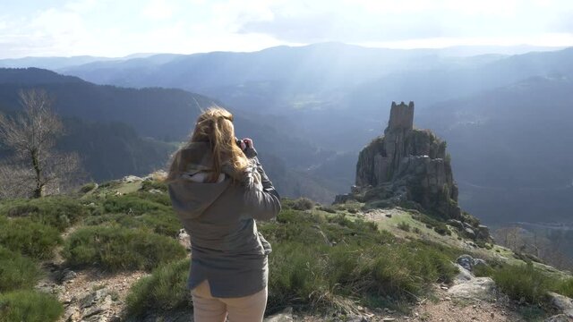 Slow motion shot of young woman photographing medieval tower ruins built on a rock, France