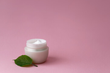 A jar of cream on a pink background near a green leaf. Natural cosmetic.