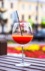 Close up of an enticing cold glass of vegetable juice with a straw on cafe table. Out of focus city center background.