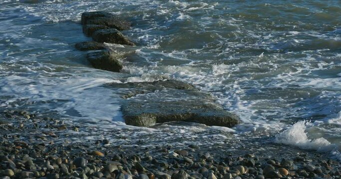 Sea surf on rocky beach. Tranquil natural background at sunny day. Black sea, Sochi, Russia.