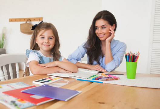 Smiling mother and daughter preparing for lessons and draws at the table with pencils and paints. Parent and pupil of preschool. First day of fall autumn. Girl from elementary class, back to school