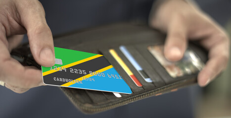Pulling plastic bank card with flag of Tanzania out of the wallet, fictional card number
