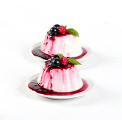 Panna cotta cream with berry sauce and fresh raspberries and black currants on a white background