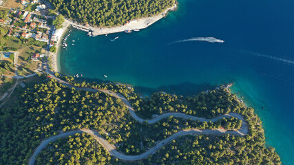 Aerial top down photo of snake road covered in pine trees leading to famous and picturesque small fishing village of Agnontas, Skopelos island, Sporades, Greece