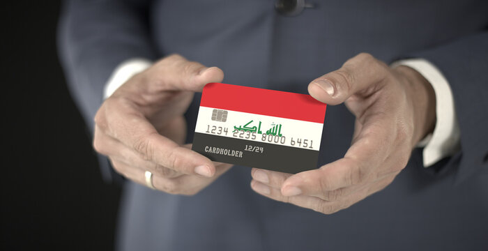 Businessman holding plastic bank card with printed flag of Iraq, fictional numbers - Powered by Adobe