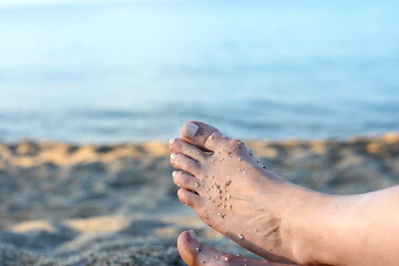 Fototapeta na wymiar Closeup image of legs of senior woman sitting relaxed on sandy beach. Mature woman feet.