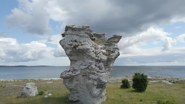 Single column-like Rauk landform by coastline with dramatic cloudy sky, circle pan