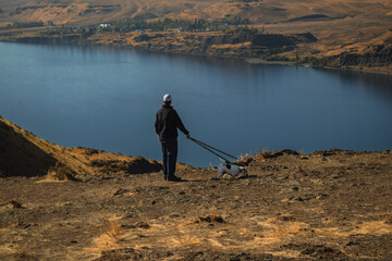 Man Walking Dogs, Overlooking Giant Lake and Rocky Landscape