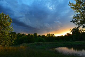 Storm Clouds and Sunset Overlooking Pond and Green Landscape