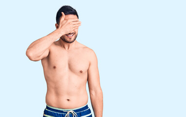 Young handsome man wearing swimwear smiling and laughing with hand on face covering eyes for surprise. blind concept.