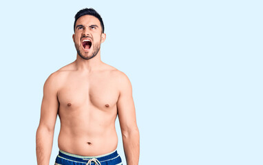 Fototapeta na wymiar Young handsome man wearing swimwear angry and mad screaming frustrated and furious, shouting with anger. rage and aggressive concept.