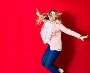 Young beautiful caucasian businesswoman wearing jacket and glasses smiling happy. Jumping with smile on face over isolated red background