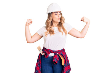 Young caucasian woman wearing security helmet showing arms muscles smiling proud. fitness concept.