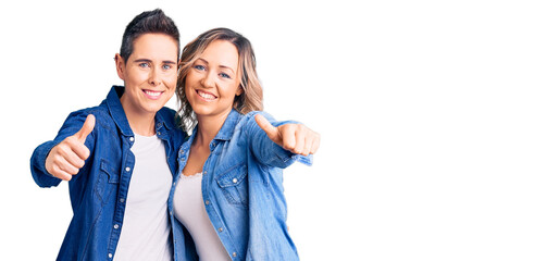 Couple of women wearing casual clothes approving doing positive gesture with hand, thumbs up smiling and happy for success. winner gesture.